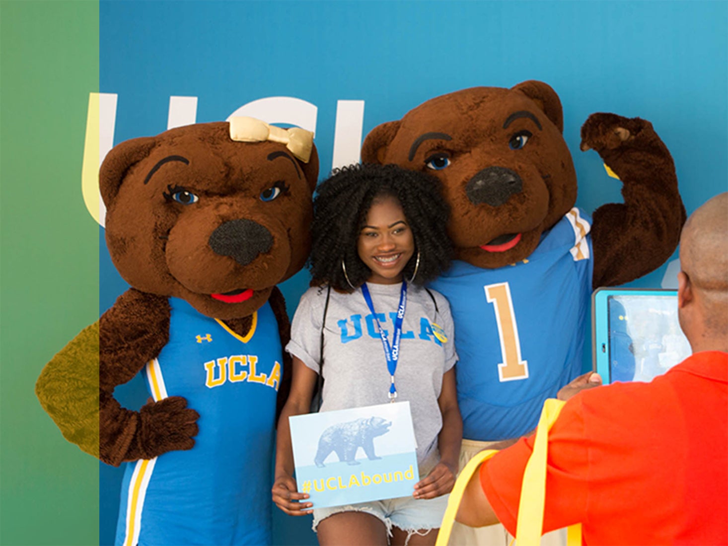 A female student holding a #UCLAbound sign poses with Joe and Josie Bruin.