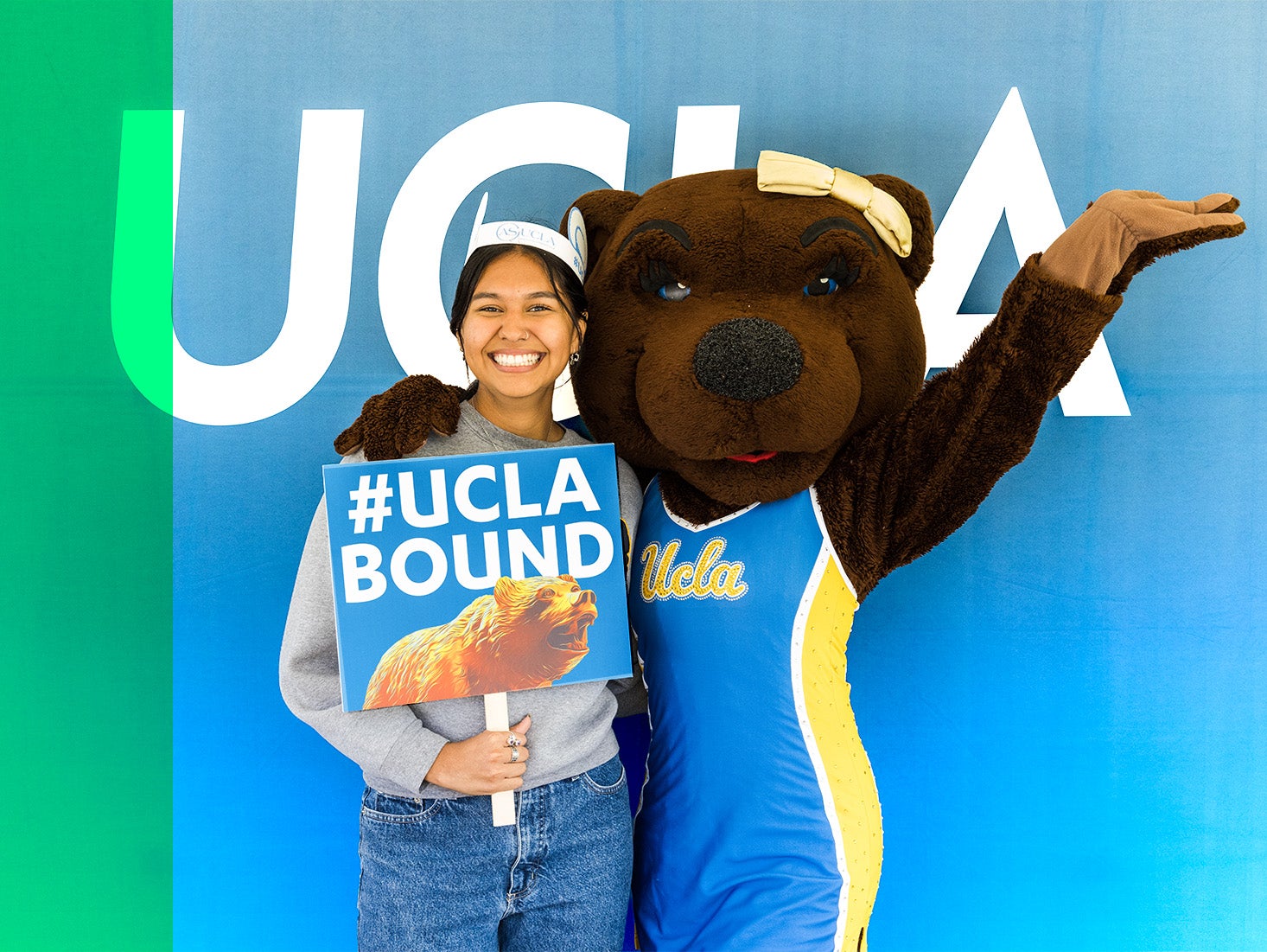 A future Bruin smiles as she holds up a UCLA Bound sign while posing with Josie Bruin.