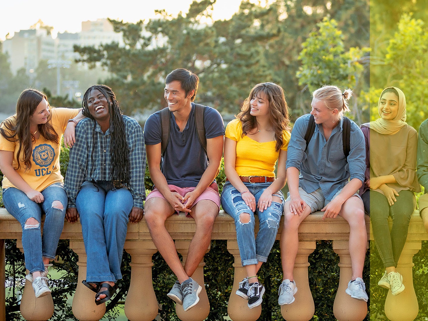 A diverse group of students sits together on a low wall.