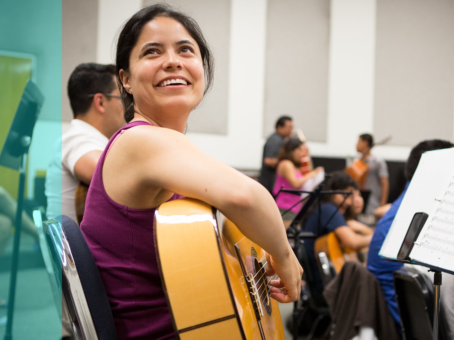 A music minor playing her guitar in a class smiles up at someone off-camera.