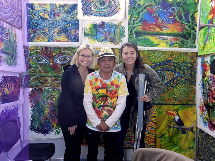 Dos estudiantes posan con un artista local y su trabajo en Perú.