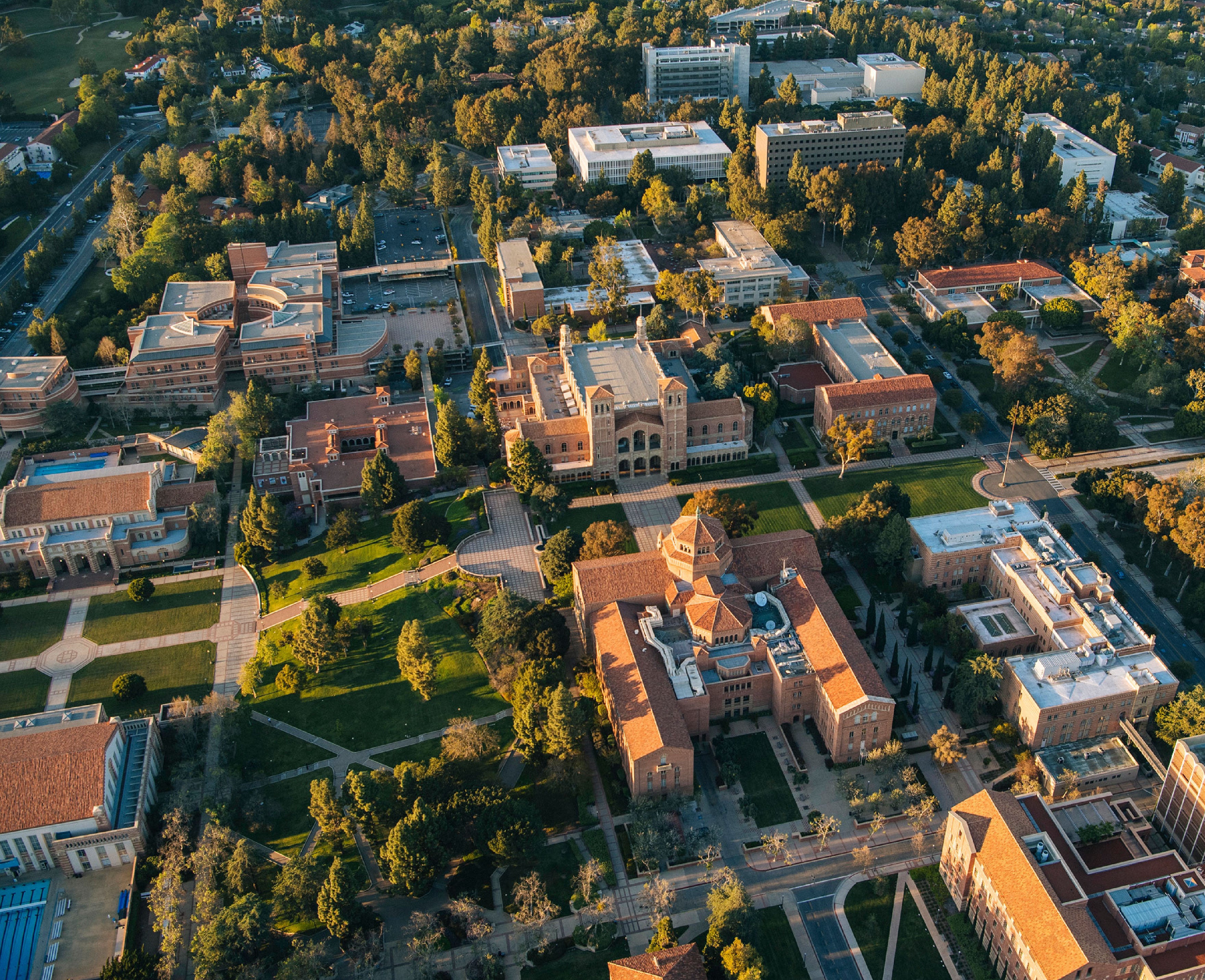 Una vista aérea del campus de UCLA, donde se muestran sus edificios, espacios verdes y caminos. La imagen captura el diseño de la universidad en la luz cálida de la tarde.