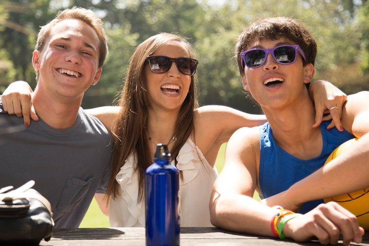 Tres estudiantes disfrutan de su compañía en una mesa al aire libre.