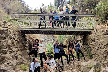 Students on a hike pause for a picture by a footbridge that spans some rocks.