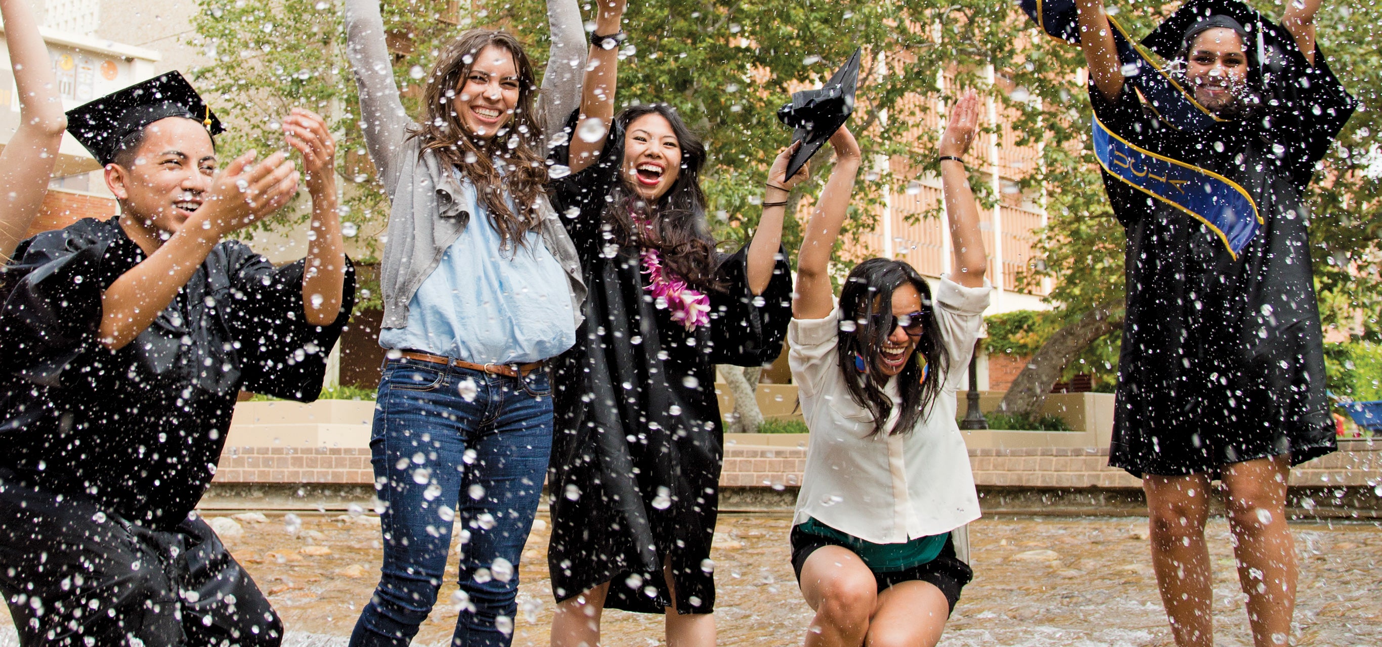 A few graduates celebrate their accomplishments by jumping in a fountain.