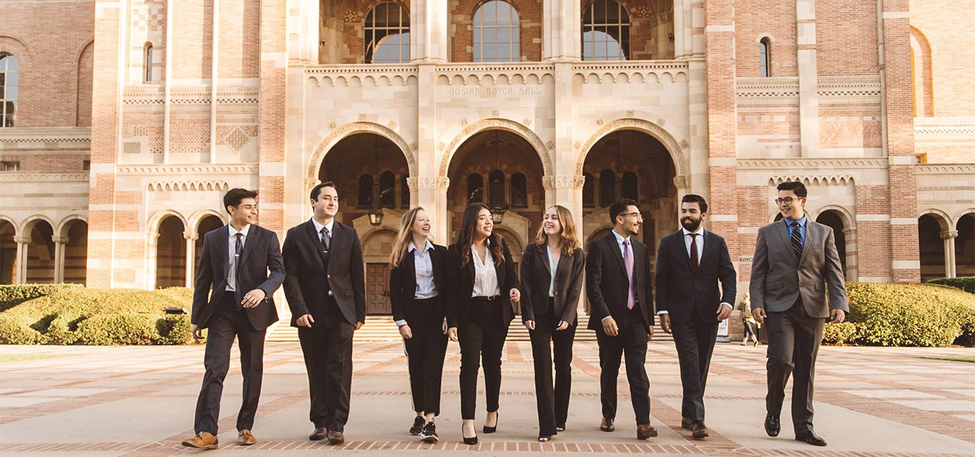 Estudiantes de Economía de la Empresa vestidos de traje pasean juntos frente al Royce Hall.