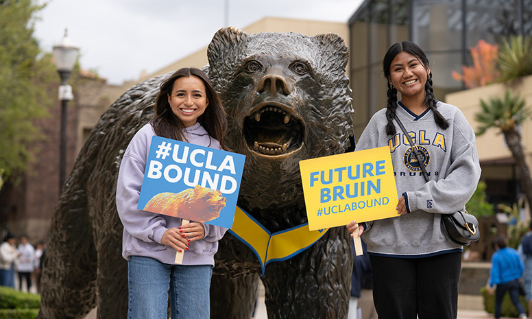 A happy student and her mom hold up UCLA-bound signs while posing with The Bruin statue.