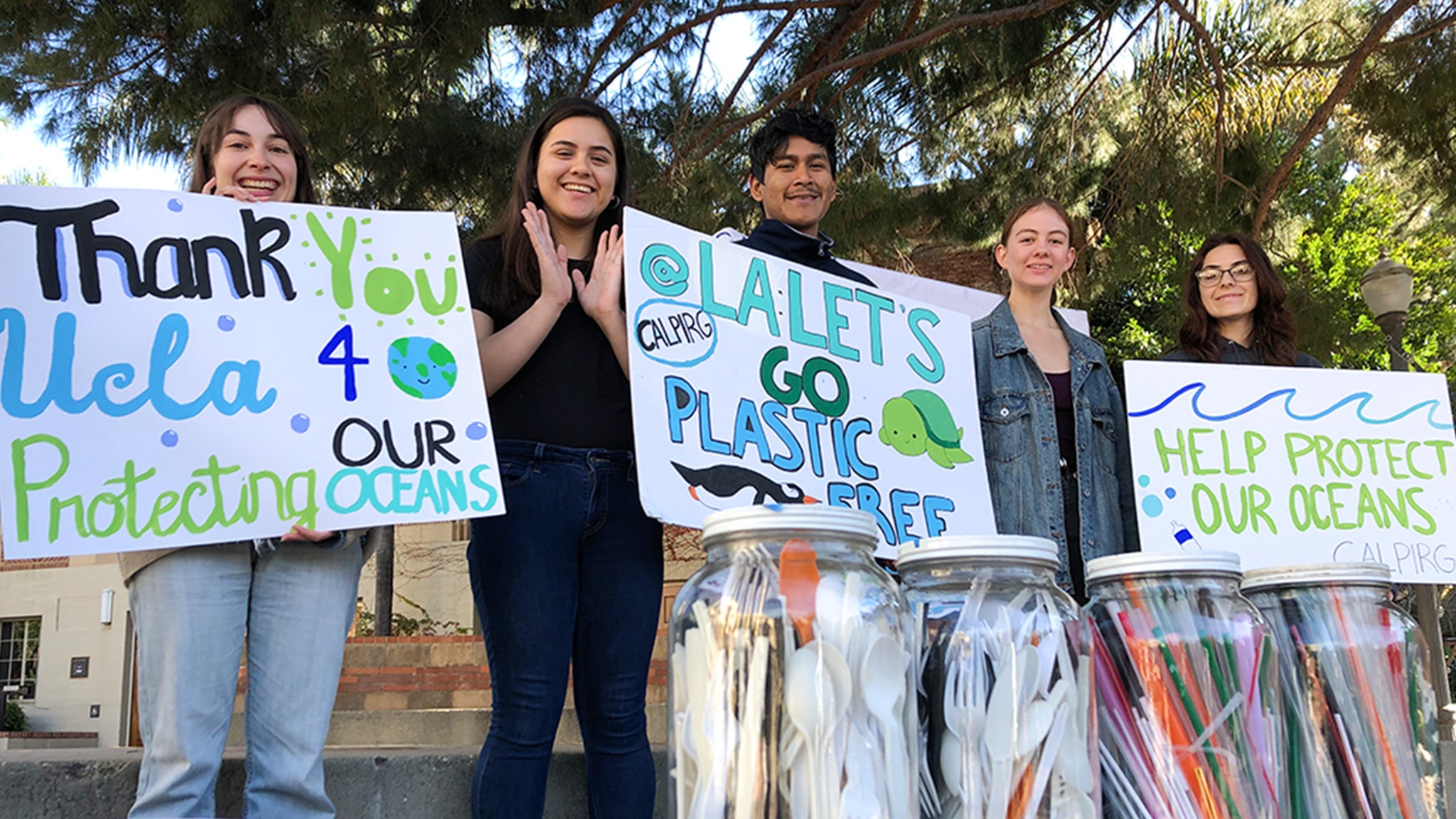 Students hold signs that encourage phasing out single-use plastic utensils and straws.