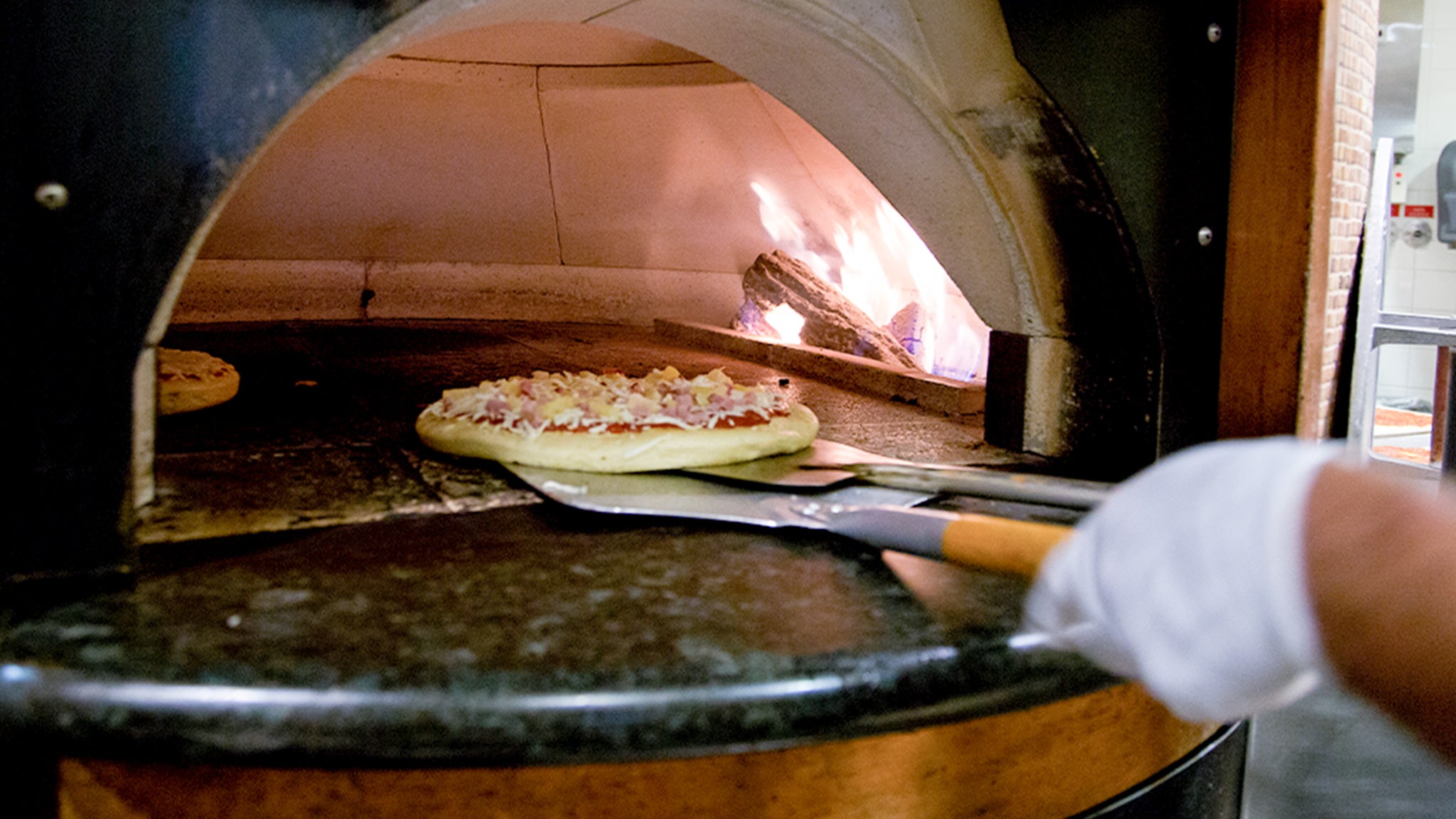 A chef slides a pizza close to the flame in the pizza oven.