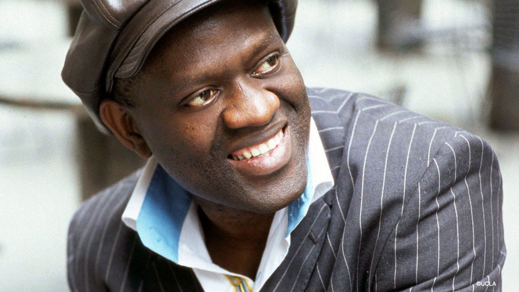 Alain Mabanckou mira hacia un lado mientras sonríe.