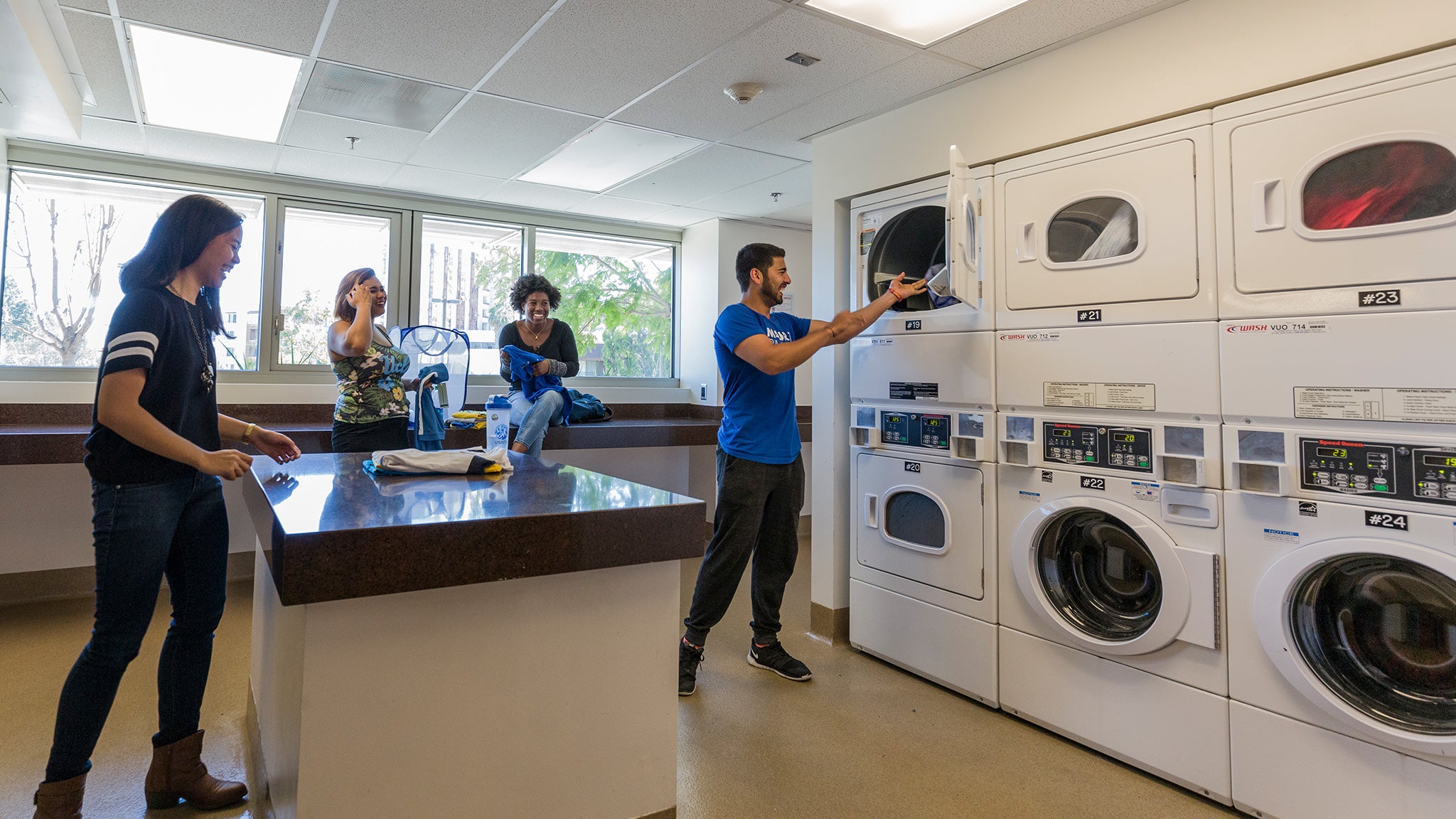 A few students who are doing laundry hang out together in a laundry room.